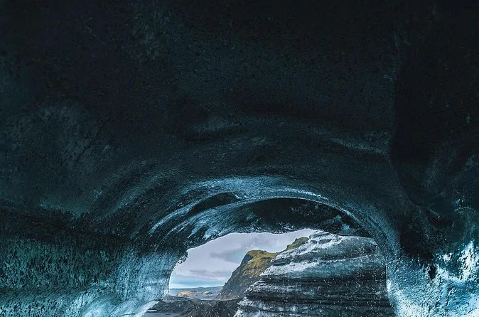 A dark ice cave arch with daylight shining in from beyond