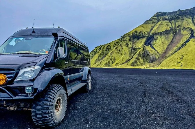 A black 4x4 van on black sand with a green mountain behind